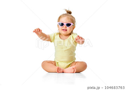 Cheerful, happy, little girl, toddler in yellow costume and sunglasses sitting on floor and smiling against white studio background 104683763