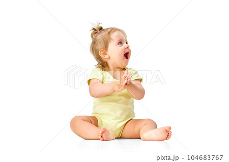 Joyful, happy little baby girl, child sitting on floor, capping hands and laughing against white studio background Joyful, happy little baby girl, child sitting on floor, capping hands and laughing against white studio background 104683767