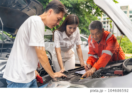 Car machanic showing the man and woman the problem of their car's engine while parking on the side of a road Car machanic showing the man and woman the problem of their car's engine while parking on the side of a road 104686592