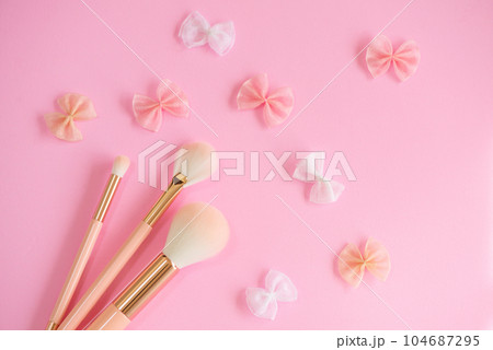 ピンク色の背景に並べたメイクブラシ3種とリボンモチーフ 104687295