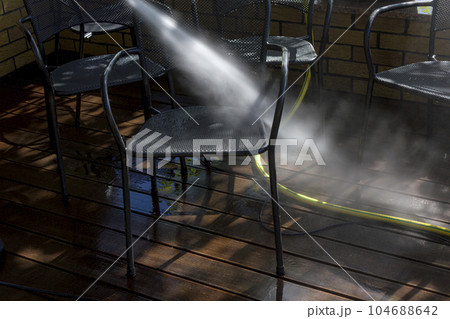Power surface washing. Man cleaning terrace with a power washer. High water pressure cleaner on wooden terrace surface and outdoor furniture. 104688642