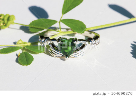 Claddagh ring with green emerald. Traditional Irish ring in shape of two hands holding a heart shaped green gemstone. Symbol of love, loyalty and friendship. Claddagh ring with green emerald. Traditional Irish ring in shape of two hands holding a heart shaped green gemstone. Symbol of love, loyalty and friendship. 104690876