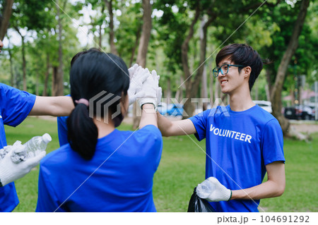Volunteers of various nationalities are showing solidarity, donating their personal time, holding black trash bags to collect plastic waste for recycling to reduce pollution in a public park 104691292