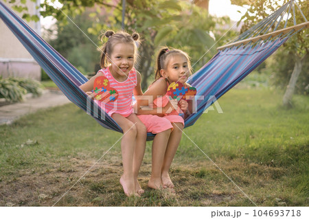 Charming hilarious sisters have fun in yard on hanging hammock Charming hilarious sisters have fun in yard on hanging hammock 104693718