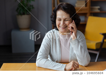 Happy middle aged senior woman talking on smartphone with family friends. Older mature lady with cell phone chatting with grown up children, resting in at home. Older generation modern tech usage 104695604