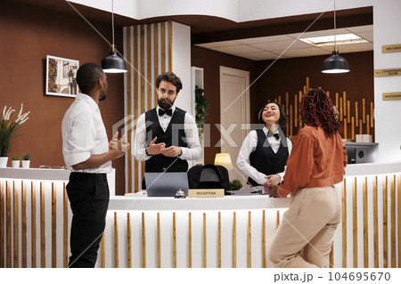 Diverse workers helping hotel guests, working at reception desk and providing advice for tourists in lobby area. Resort staff doing check in registration on computer, accommodation service. Diverse workers helping hotel guests, working at reception desk and providing advice for tourists in lobby area. Resort staff doing check in registration on computer, accommodation service. 104695670