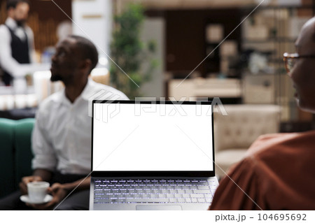 Tourist using white screen on pc sitting in lounge area at hotel lobby, checking blank copyspace with chroma key. Female guest holding laptop with isolated display at resort reception. 104695692