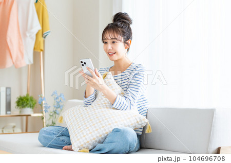 リビングでスマホを見る若い女性 104696708