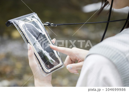 川辺で防水スマホケースに入れたスマホを操作する若い女性手元 104699986