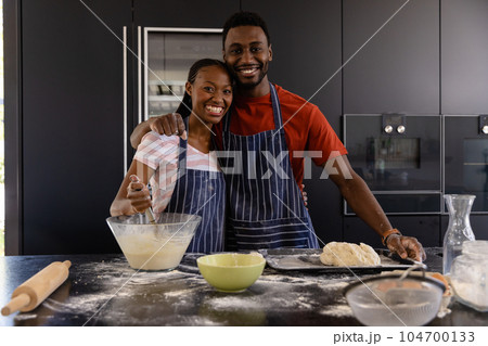 Portrait of happy african american couple in aprons preparing bread dough in kitchen 104700133