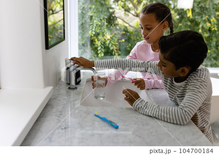 Biracial brother and sister in pyjamas brushing teeth together in the morning in bathroom 104700184
