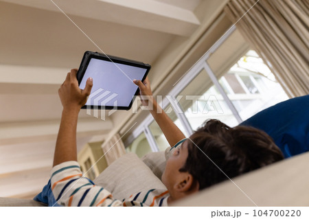 Low angle of happy biracial boy lying on couch using tablet with copy space on screen in living room Low angle of happy biracial boy lying on couch using tablet with copy space on screen in living room 104700220