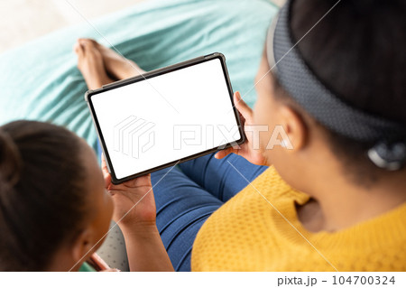 African american mother and daughter sitting on bed and using tablet with copy space 104700324