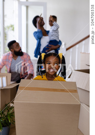 Smiling african american daughter and father carrying boxes with family in background at new home 104700338