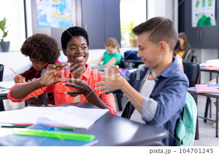Happy, diverse female school teacher and boy practicing sign language in class 104701245