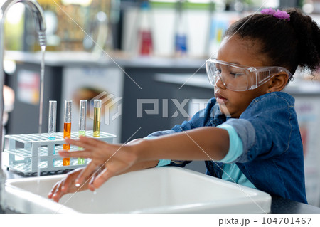 Biracial schoolgirl in safety glasses washing hands in science class 104701467