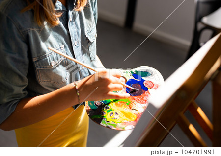 Happy caucasian schoolgirl painting using brush and easel in school art class Happy caucasian schoolgirl painting using brush and easel in school art class 104701991