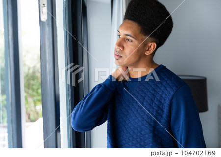 Thoughtful biracial man standing in bedroom looking out of window Thoughtful biracial man standing in bedroom looking out of window 104702169