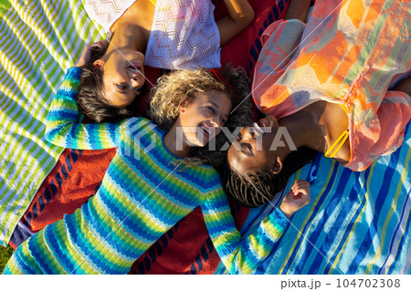 Happy diverse female friends lying on towels and smiling in garden 104702308
