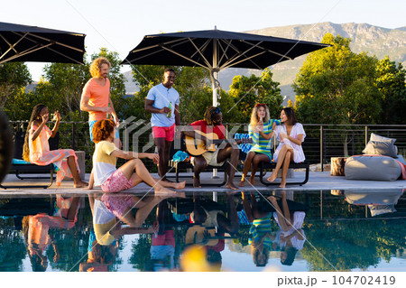 Happy diverse group of friends having pool party and playing guitar in garden 104702419