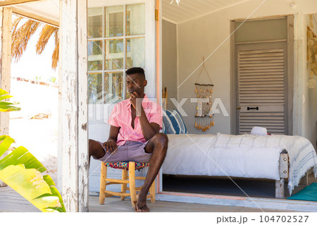 Thoughtful biracial man looking away sitting on porch at summer beach house, copy space 104702527
