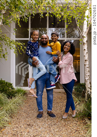 Portrait of happy biracial parents holding son and daughter in garden outside house, copy space 104702681