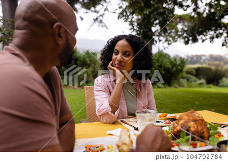 Happy biracial couple having meal and talking sitting at table in garden Happy biracial couple having meal and talking sitting at table in garden 104702784