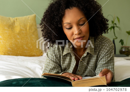 Biracial woman reading book lying on bed in bedroom 104702978