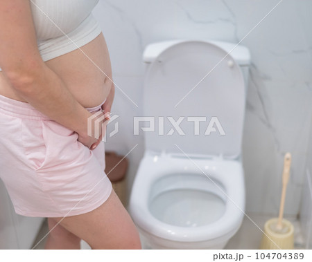 Pregnant woman holding her belly in the toilet. incontinence during pregnancy.  104704389