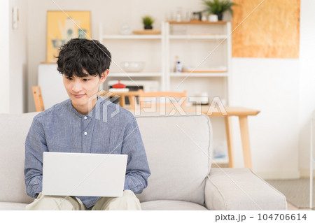 ソファーに座ってノートパソコンを膝の上において操作する若い男性 ソファーに座ってノートパソコンを膝の上において操作する若い男性 104706614