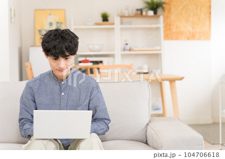 ソファーに座ってノートパソコンを膝の上において操作する若い男性 ソファーに座ってノートパソコンを膝の上において操作する若い男性 104706618