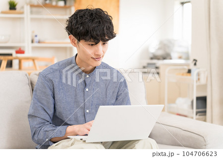 ソファーに座ってノートパソコンを膝の上において操作する若い男性 ソファーに座ってノートパソコンを膝の上において操作する若い男性 104706623
