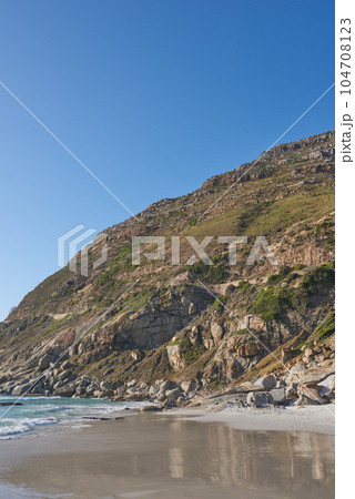 Beautiful view of a nature landscape with the sea, sand, and a blue sky background. Natural outdoors setting of the beach and green mountains. Isolated environment outside near ocean water. Beautiful view of a nature landscape with the sea, sand, and a blue sky background. Natural outdoors setting of the beach and green mountains. Isolated environment outside near ocean water. 104708123