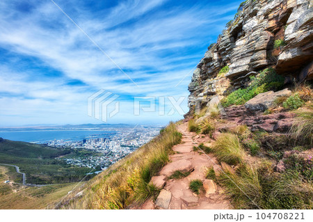 Beautiful scenic view of mountains and a hiking or walking trail surrounded by foliage, plants and greenery on a sunny spring day. Landscape covered in rocks and flora with cloudy blue sky copy space Beautiful scenic view of mountains and a hiking or walking trail surrounded by foliage, plants and greenery on a sunny spring day. Landscape covered in rocks and flora with cloudy blue sky copy space 104708221