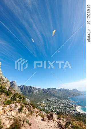People paragliding from a mountain with a scenic view in summer. Tourists having fun and doing adventurous activities while on holiday in a clear blue sky. People hand gliding from a cliff in nature People paragliding from a mountain with a scenic view in summer. Tourists having fun and doing adventurous activities while on holiday in a clear blue sky. People hand gliding from a cliff in nature 104708910