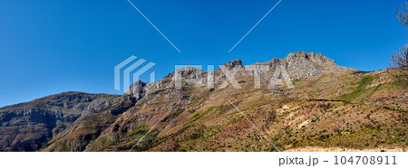 Twelve Apostles at Table Mountain in Cape Town against a blue sky background from below. Breathtaking view of plants and shrubs growing around a majestic rocky valley and scenic landmark in nature Twelve Apostles at Table Mountain in Cape Town against a blue sky background from below. Breathtaking view of plants and shrubs growing around a majestic rocky valley and scenic landmark in nature 104708911