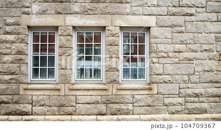 Old windows on the side of a brown stone building for architectural detail. Closeup of the cultural and textured design on a brick wall outside of a house, school or church in a small town Old windows on the side of a brown stone building for architectural detail. Closeup of the cultural and textured design on a brick wall outside of a house, school or church in a small town 104709367