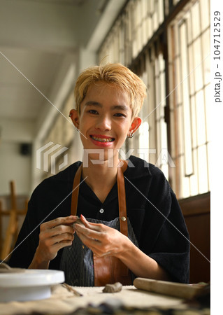 Delighted asian man kneading clay for creating pottery ceramics. Handicraft, creativity and hobby concept Delighted asian man kneading clay for creating pottery ceramics. Handicraft, creativity and hobby concept 104712529