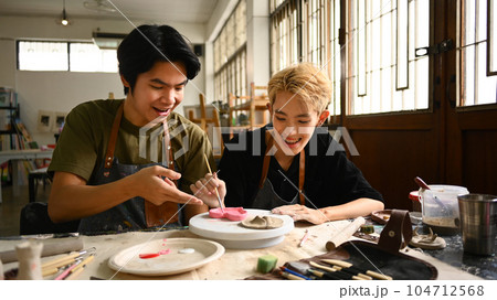Joyful young asian gay couple creating handmade ceramics in art class. LGBTQ, indoors lifestyle activity concept 104712568