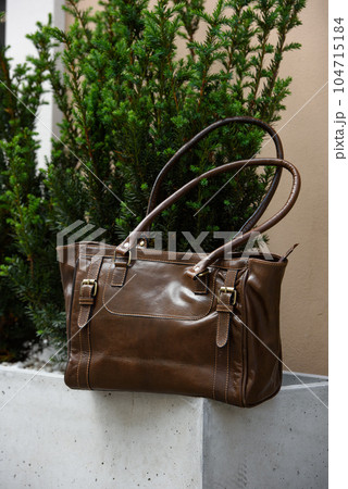 close-up photo of brown leather bag on a flowerpot made of cement. outdoors photo 104715184