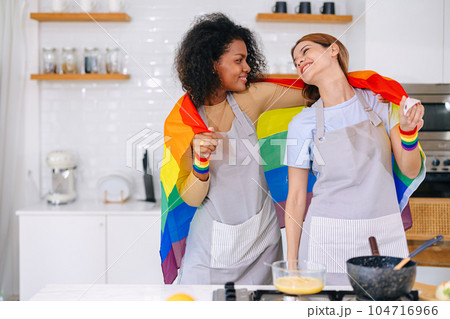 LGBT couple women happy celebrate pride month together with rainbow flag in kitchen cooking at home LGBT couple women happy celebrate pride month together with rainbow flag in kitchen cooking at home 104716966