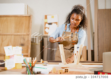 African black woman carpenter joiner working build wooden chair handcraft furniture in wood studio workshop. African black woman carpenter joiner working build wooden chair handcraft furniture in wood studio workshop. 104717008