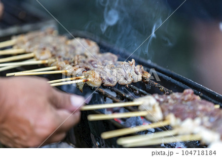 Arranged pork skewers grilled on a hot stove. smoke floating above There is a blurry hand foreground. Selective focus. It is a delicious and popular street food in Thailand. Arranged pork skewers grilled on a hot stove. smoke floating above There is a blurry hand foreground. Selective focus. It is a delicious and popular street food in Thailand. 104718184