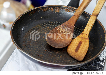 Empty black round cast iron pan with a spatula and a wooden spatula that had just finished cooking on the stove in the middle of the day Empty black round cast iron pan with a spatula and a wooden spatula that had just finished cooking on the stove in the middle of the day 104718224