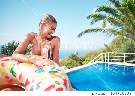 A young woman is relaxing by the pool. in the background a garden and palm trees. 104719535