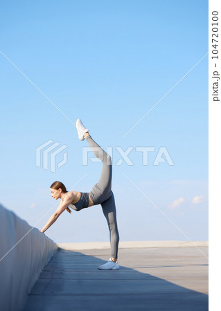 Flexibility and strength. Youn sportive woman in stylish sportswear training, doing stretching exercises outdoors on sunny day Flexibility and strength. Youn sportive woman in stylish sportswear training, doing stretching exercises outdoors on sunny day 104720100