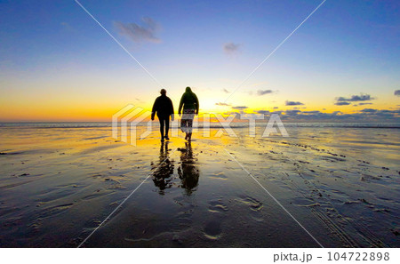 Silhouette of Two Teenage Girls Walking on Beach Under a Dramatic Sky 104722898