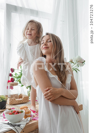 A little blonde girl with her mom on a kitchen countertop decorated with peonies. The concept of the relationship between mother and daughter. Spring atmosphere. A little blonde girl with her mom on a kitchen countertop decorated with peonies. The concept of the relationship between mother and daughter. Spring atmosphere. 104723276