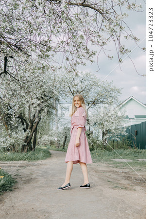 Blonde girl on a spring walk in the garden with cherry blossoms. Female portrait, close-up. A girl in a pink polka dot dress. Blonde girl on a spring walk in the garden with cherry blossoms. Female portrait, close-up. A girl in a pink polka dot dress. 104723323