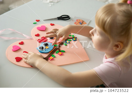 A blogger girl makes a felt craft for Valentine's Day in the shape of a heart. The concept of children's creativity and handmade. A blogger girl makes a felt craft for Valentine's Day in the shape of a heart. The concept of children's creativity and handmade. 104723522